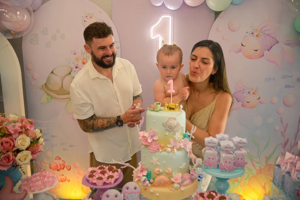 Criança de 1 ano em sua festa de aniversario infantil com os pais, onde eles assompram a velinha de 1 ano, na qual o tema é fundo do mar.